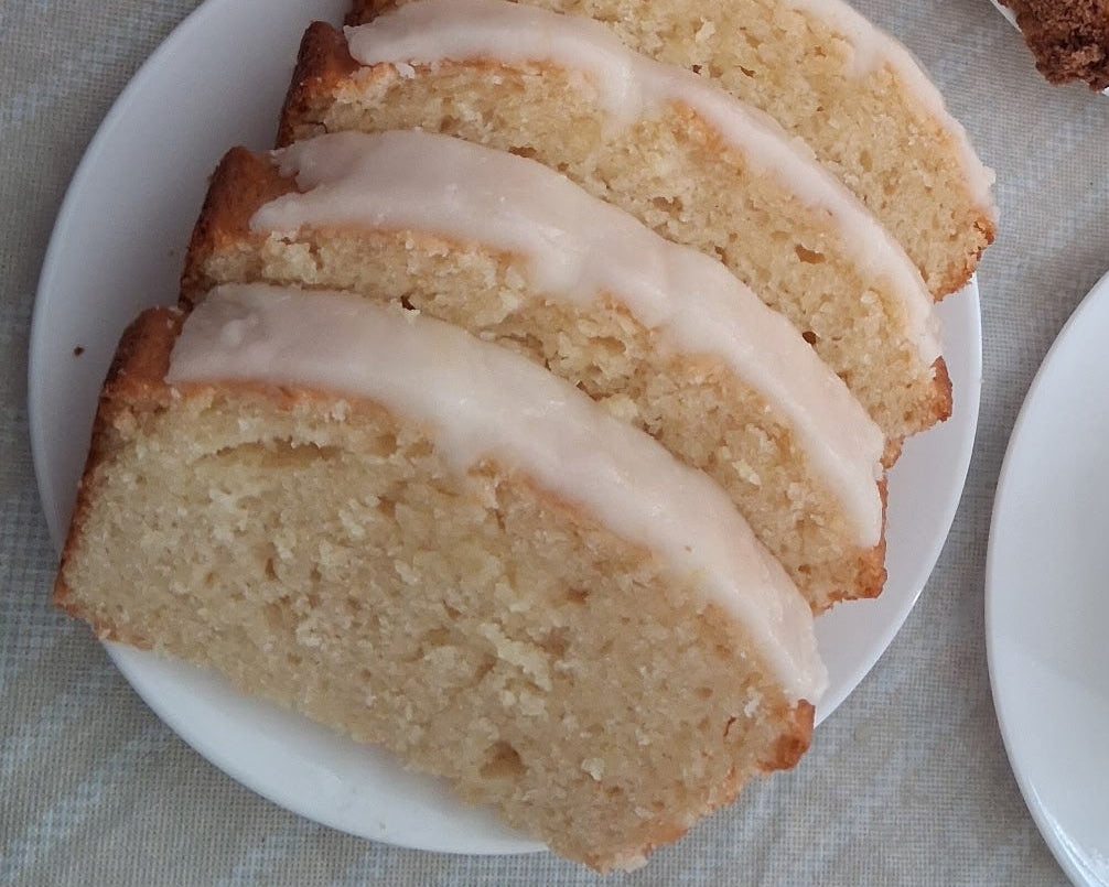 Four slices of a light golden-brown loaf cake with a pale pink icing, served on a white plate.